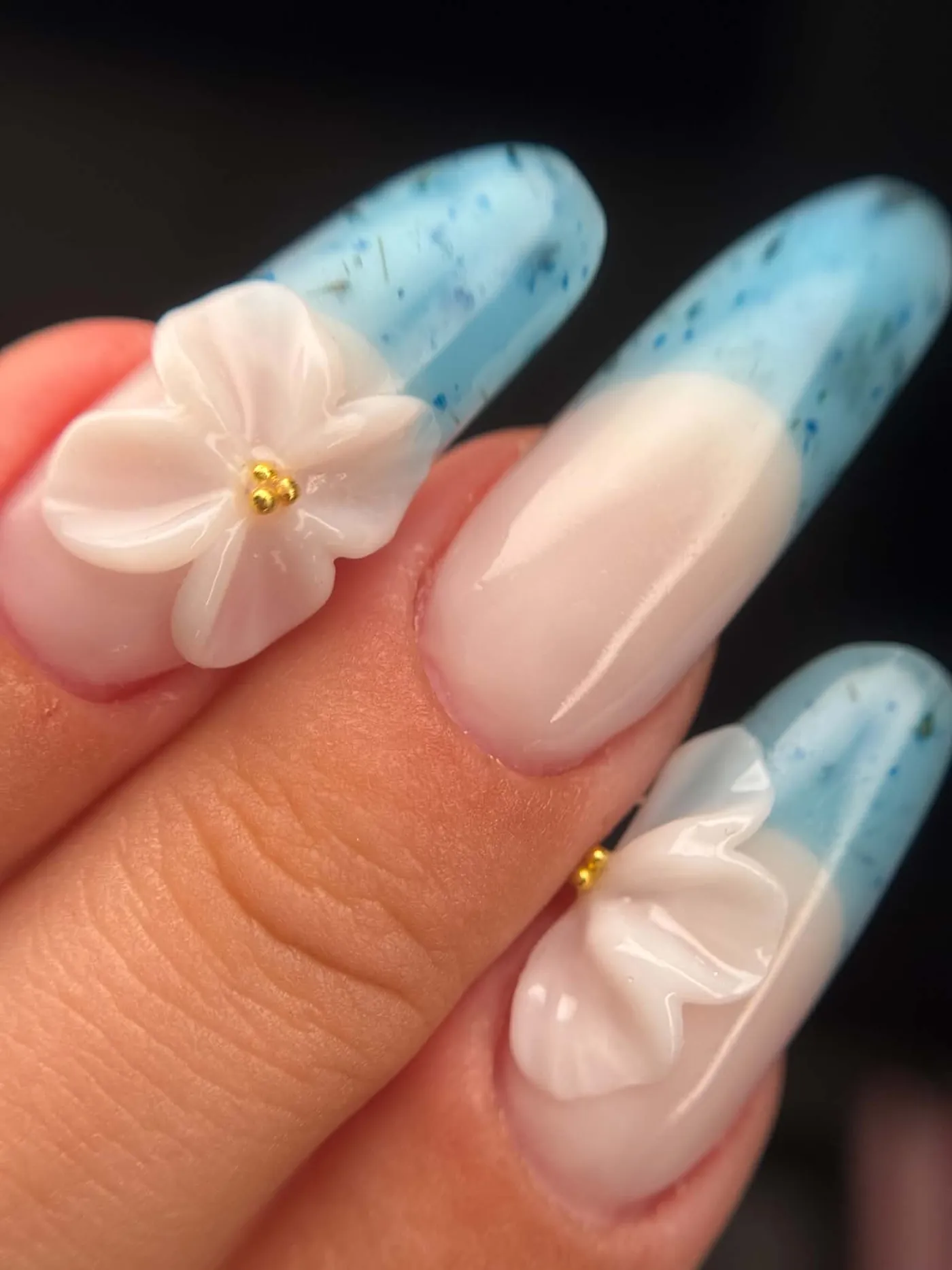 Zbliżenie niebieskiego frencha z białymi kwiatami 3D i złotymi drobinkami — OZAYA Nails Kraków